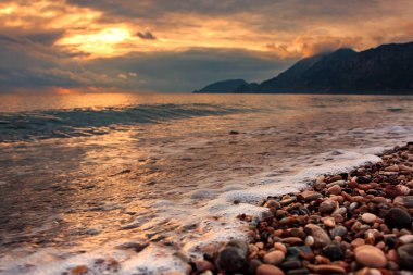Akdeniz 'in kayalık kıyılarında, 1 Ocak 2022' de Türkiye 'nin Antalya kentindeki dağların arka planına karşı güzel bir günbatımında dalgalar var..