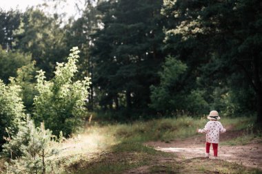 Küçük bir kız açık, güneşli bir yaz gününde bir patika boyunca yürür..