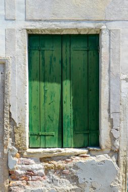 Green window on cracked concrete wall overlooking red bricks in Burano Island, Italy