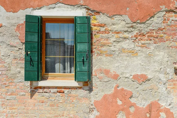 オレンジの古い家の壁の上の緑の窓イタリアのブラーノ島の具体的な可視赤レンガの亀裂 — ストック写真
