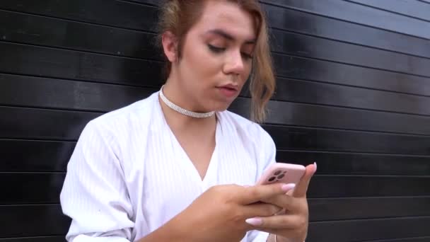 Handsome young using phone in her hands chating leaning on black gate in the street thinking — Stock Video