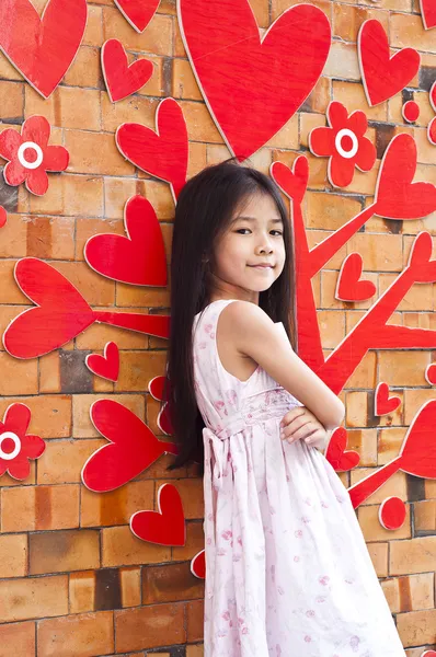 亚洲小姑娘假扮与红色的心形装饰砖的墙上. — 图库照片