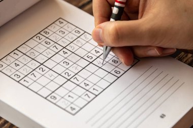 Mekanik kalem kullanarak sudoku bulmacası çözen bir kişi.