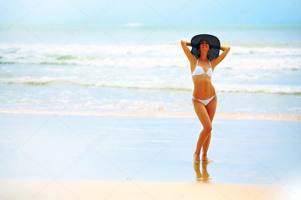Beautiful woman in bikini and big hat posing on the beach