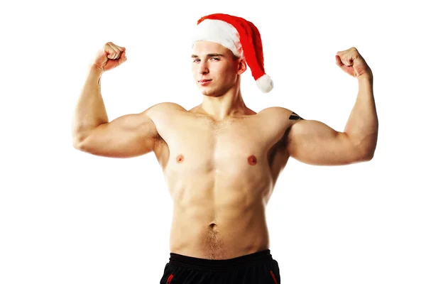 Young muscular man wearing Christmas Santa hat demonstrate his muscles. — Stock Photo, Image
