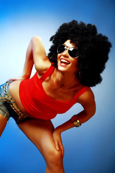 Smiling tanned woman with afro hair posing against blue background — Stock Photo, Image