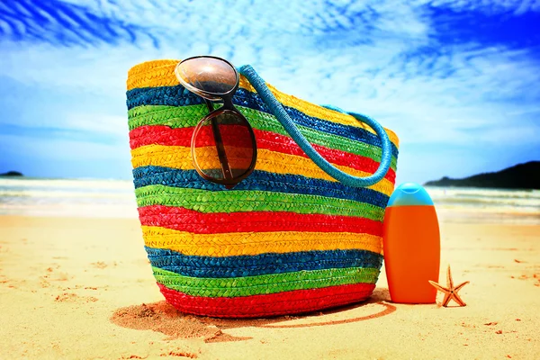 Kleurrijke stro tas, zonnebril, fles zon lotion en zeester op tropische paradijs strand — Stockfoto