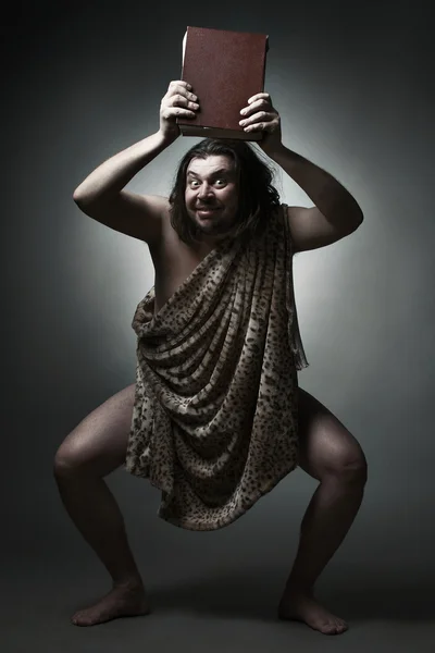 Caveman wearing leopard skin hold big book over head. — Stock Photo, Image