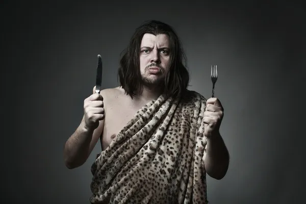 Hombre salvaje hambriento con piel de leopardo sujetar tenedor y cuchillo . — Foto de Stock