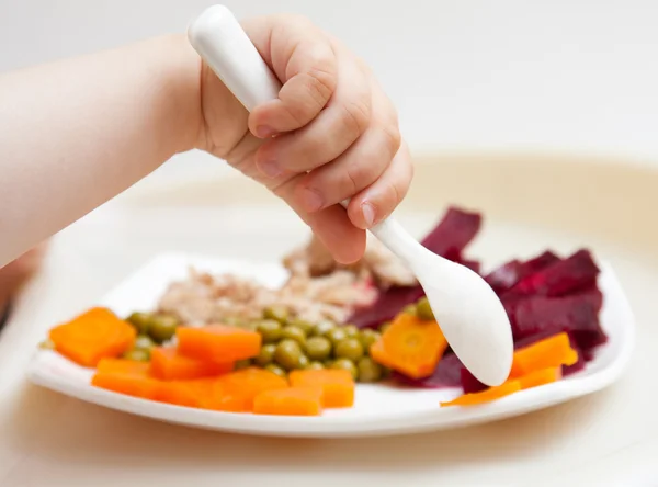Рука малыша с ложкой и тарелка с овощами — стоковое фото
