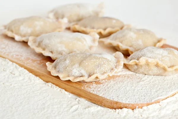 Dumplings (vareniki) in flour on wooden board — Stock Photo, Image