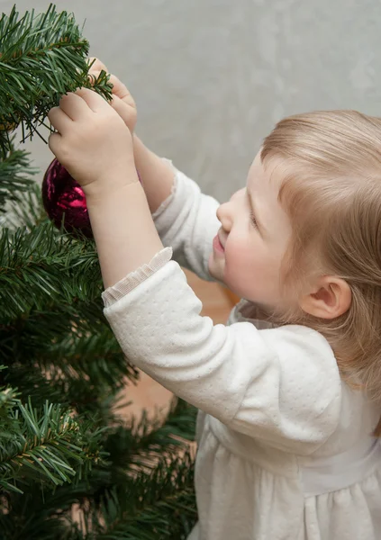 Lächelndes kleines Mädchen schmückt einen Weihnachtsbaum — Stockfoto