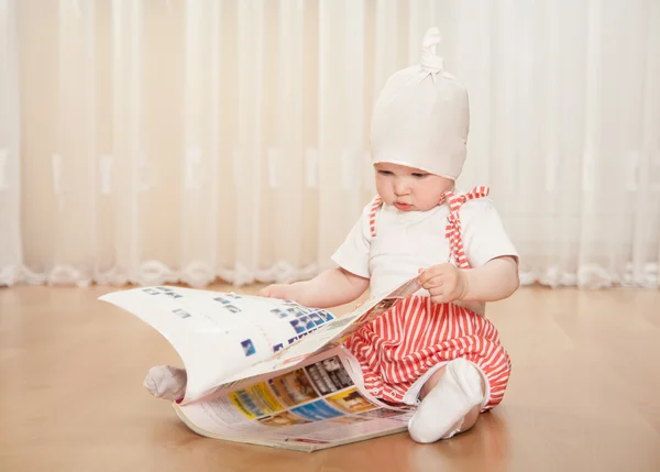 Liten flicka undersöka en stor tidning hemma — Stockfoto