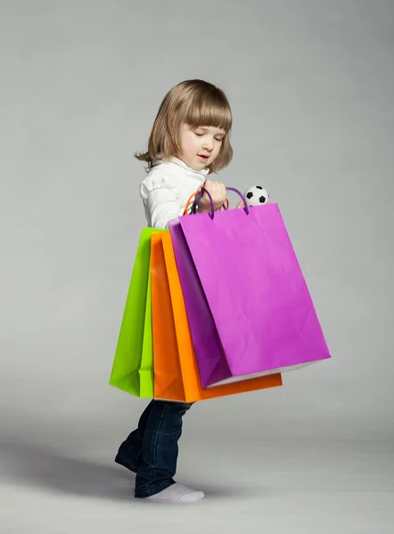 Küçük kız alışveriş torbaları ile gülümseyen — Stok fotoğraf