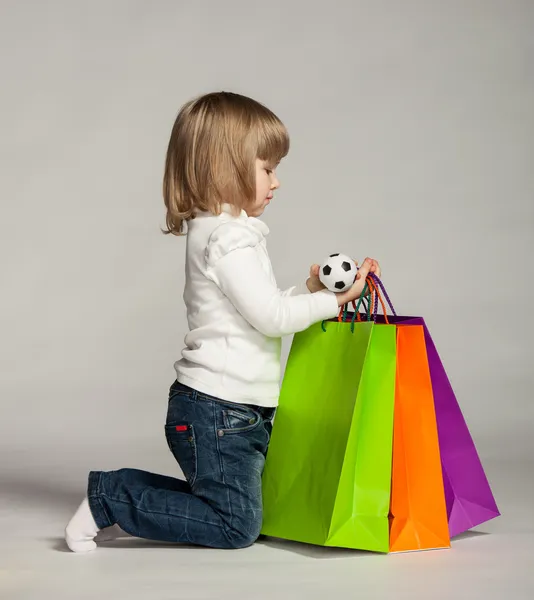 Klein meisje zitten in de buurt van shopping tassen — Stockfoto