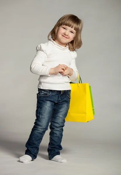 Küçük kız çok renkli alışveriş torbaları tutmak gülümseyen — Stok fotoğraf