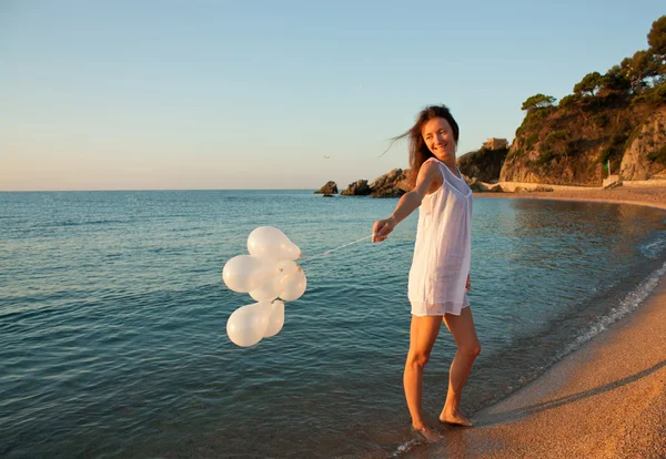 Feliz sorrindo menina morena com balões brancos na praia ensolarada — Fotografia de Stock