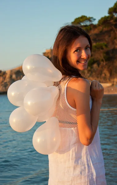 快乐的微笑黑发女孩与阳光明媚的海滩上的白色气球 — 图库照片