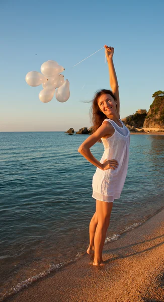 Happy smiling brunette girl with white balloons on sunny beach — Stock Photo, Image