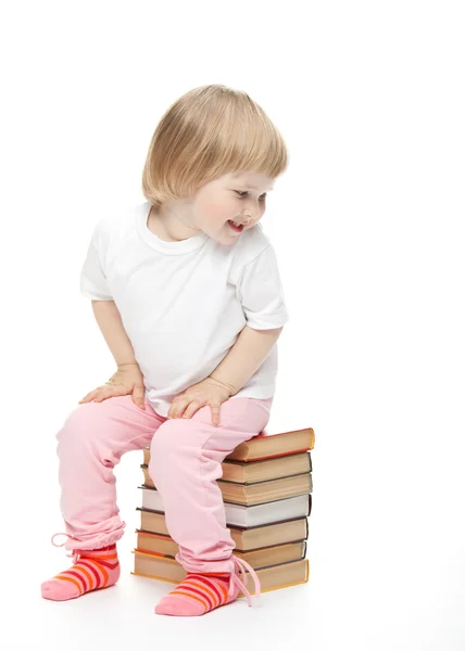 The baby girl is sitting on the books and turning back Stock Image