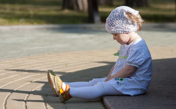 Liten flicka sitter på en trottoar — Stockfoto