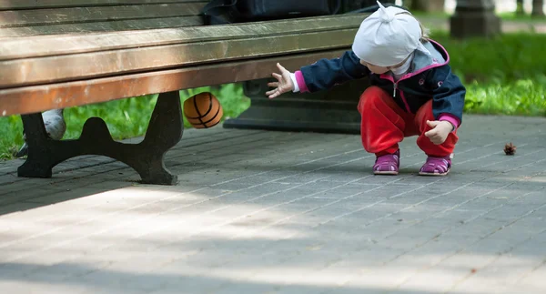 Pieni tyttö heittää pallon penkin alle — kuvapankkivalokuva