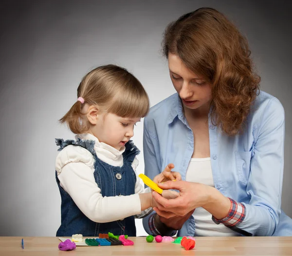 Young mother and her daughter modelling with plasticine, dark background — Stock Photo, Image