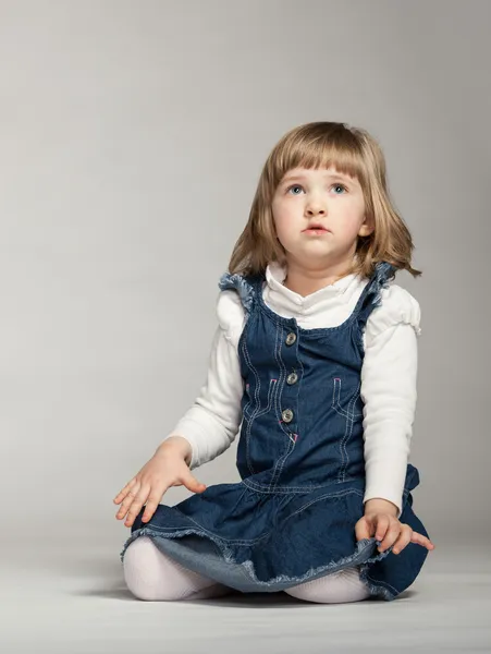 Маленькая девочка смотрит вверх и сидит на полу — стоковое фото