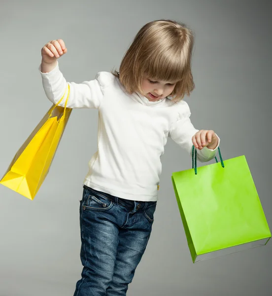 Sonriente niña mirando en bolsas de compras multicolores —  Fotos de Stock
