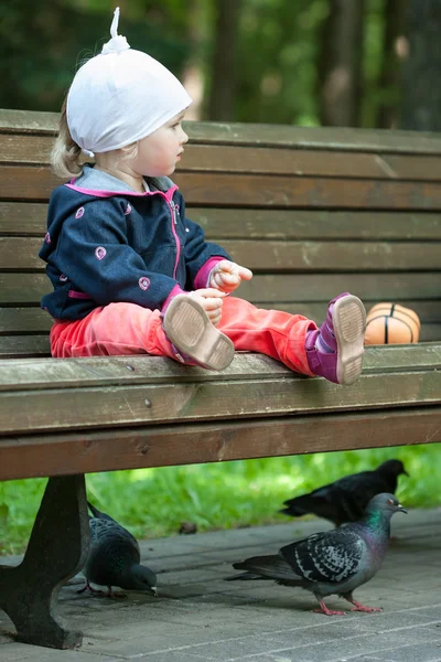 Bambina seduta su una panchina e che nutre piccioni — Foto Stock