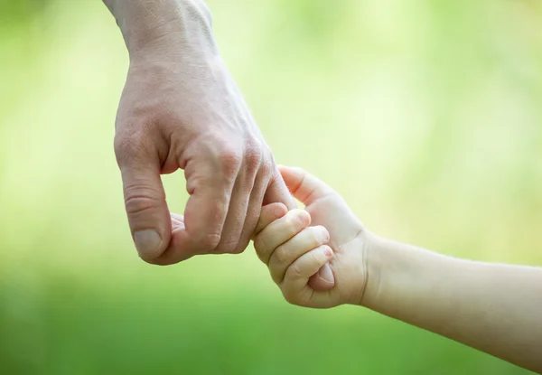 Hands of man and child holding together on light green background — Stock Photo, Image
