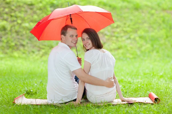 Glücklich lächelndes junges Paar unter rotem Regenschirm — Stockfoto