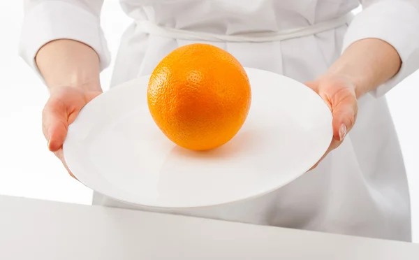Женские руки показывают спелый апельсин на тарелке — стоковое фото