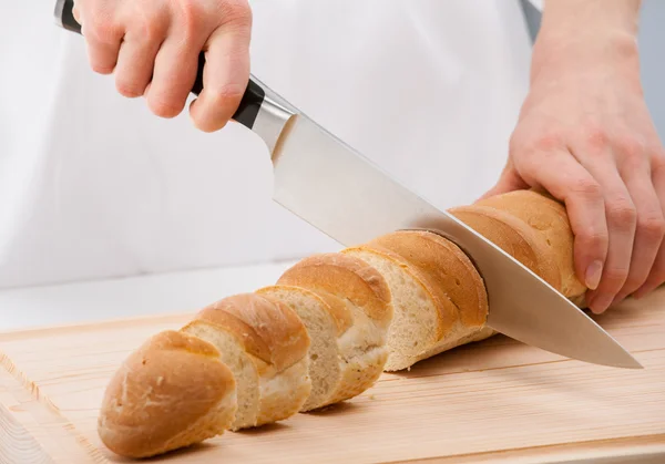 Cook cutting bread on wooden board — Stock Photo, Image