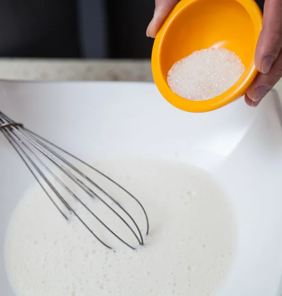 Die menschliche Hand fügt dem aufgeschäumten Eiweiß Zucker hinzu — Stockfoto