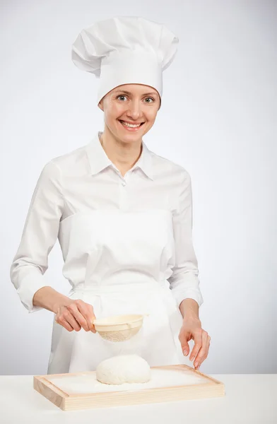 Young female cook powdering dough with flour on wooden board — Stock Photo, Image