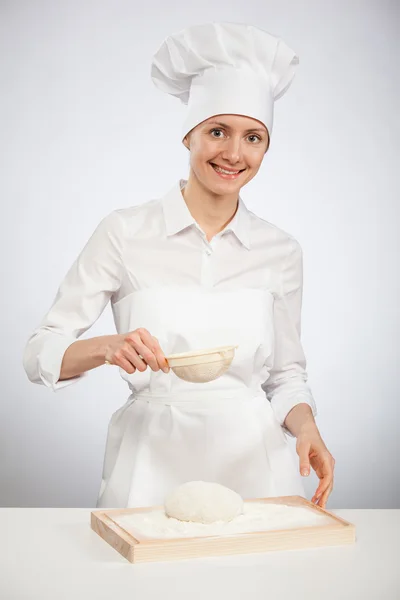 Junge Köchin pudert Teig mit Mehl auf Holzbrett — Stockfoto
