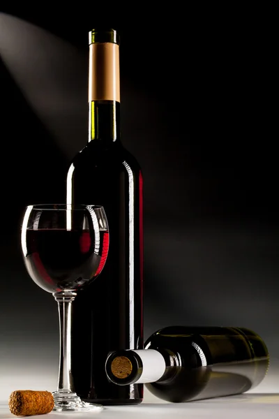 Filled glass of red wine and wine bottles — Stock Photo, Image