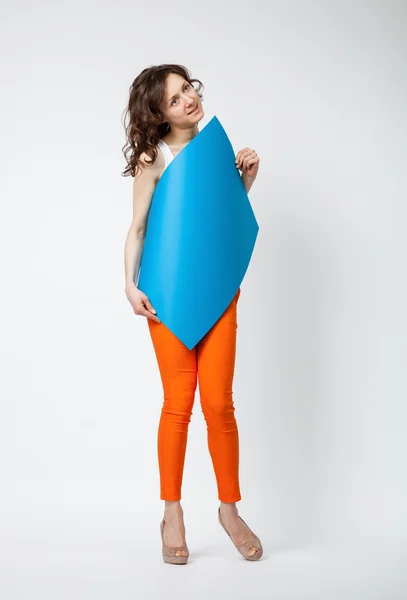 Krásná mladá žena v oranžové kalhoty drží modrý papír — Stock fotografie