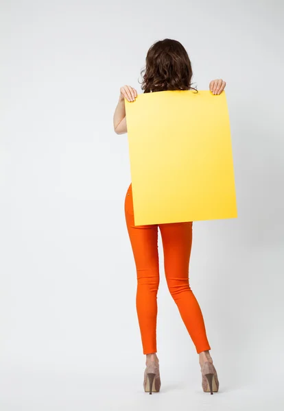 Jovem mulher em calças laranja segurando papel amarelo — Fotografia de Stock
