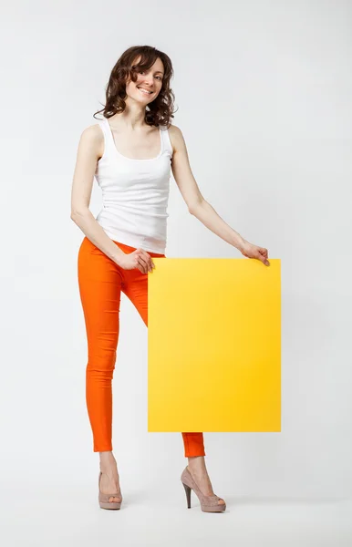 Radostné mladá žena v oranžové kalhoty drží žlutý papír — Stock fotografie