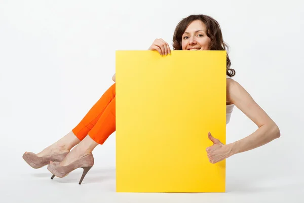 Χαρούμενη νεαρή γυναίκα στο πορτοκαλί παντελόνι κρατώντας κίτρινο χαρτί — Φωτογραφία Αρχείου