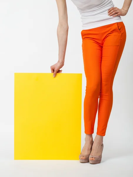 Unrecognizable young woman in orange pants holding yellow paper — Stock Photo, Image