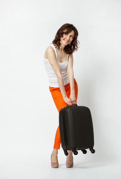 Speelse jonge vrouw in oranje broek met koffer — Stockfoto