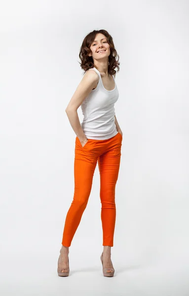 Feliz sorrindo jovem mulher em calças laranja posando em fundo neutro — Fotografia de Stock