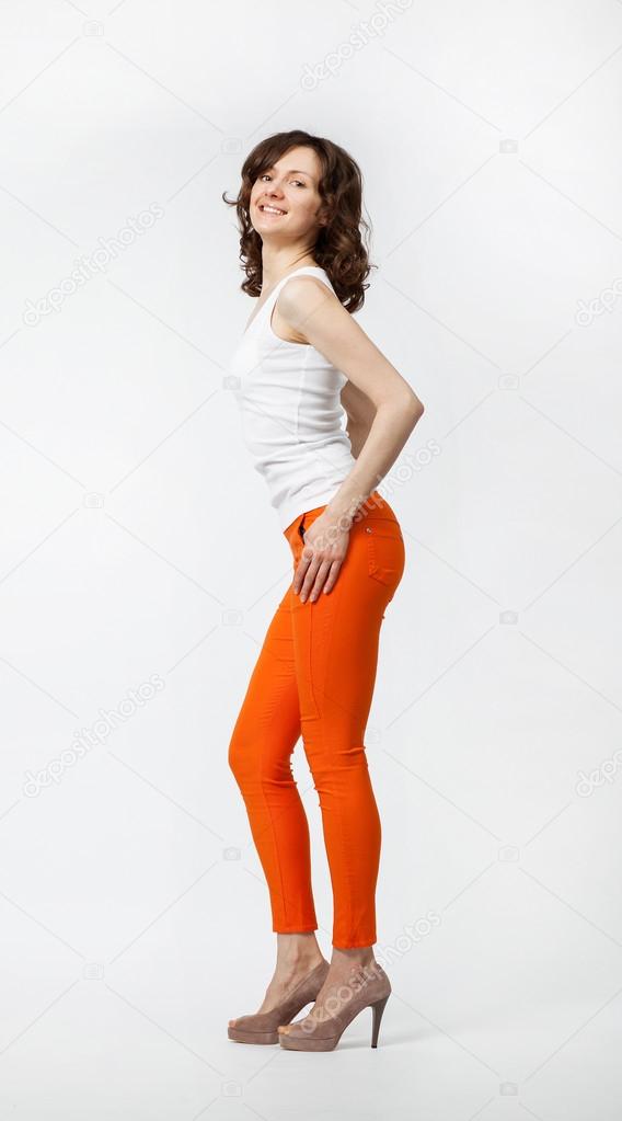 Happy smiling young woman in orange pants posing on neutral background