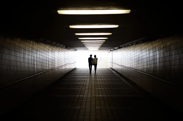 Pareja joven en silueta caminando hacia la salida del paso subterráneo peatonal —  Fotos de Stock