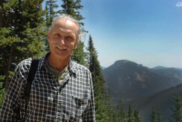 Sonriente hombre de mediana edad cerca de árboles, montañas Imagen De Stock
