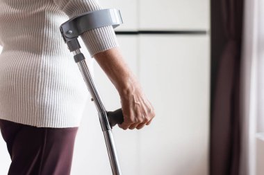 Koltuk değneklerini kullanan yaşlı bir kadın evde yürüyüş, rehabilitasyon ve iyileşme konsepti kullanıyor.