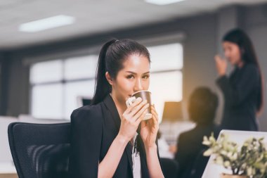 Ofiste çalışırken kahve içen güzel Asyalı kadın.